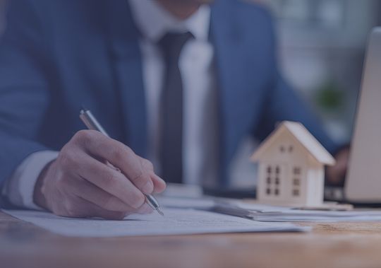 Profesional firmando contrato inmobiliario con modelo de casa y laptop en escritorio