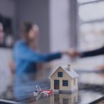 Casa en miniatura con llaves sobre mesa, simbolizando cierre de venta inmobiliaria.