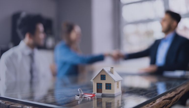 Casa en miniatura con llaves sobre mesa, simbolizando cierre de venta inmobiliaria.